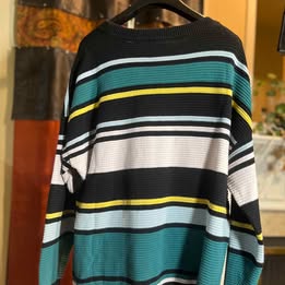 Black and teal striped sweater with white and yellow accents hanging on a hanger.
